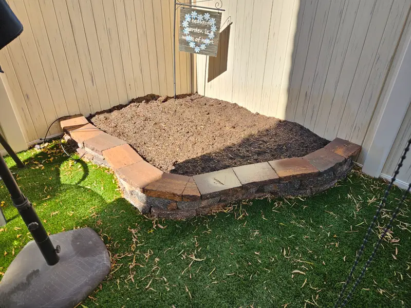 Backyard corner garden bed edged in stone beside artificial turf